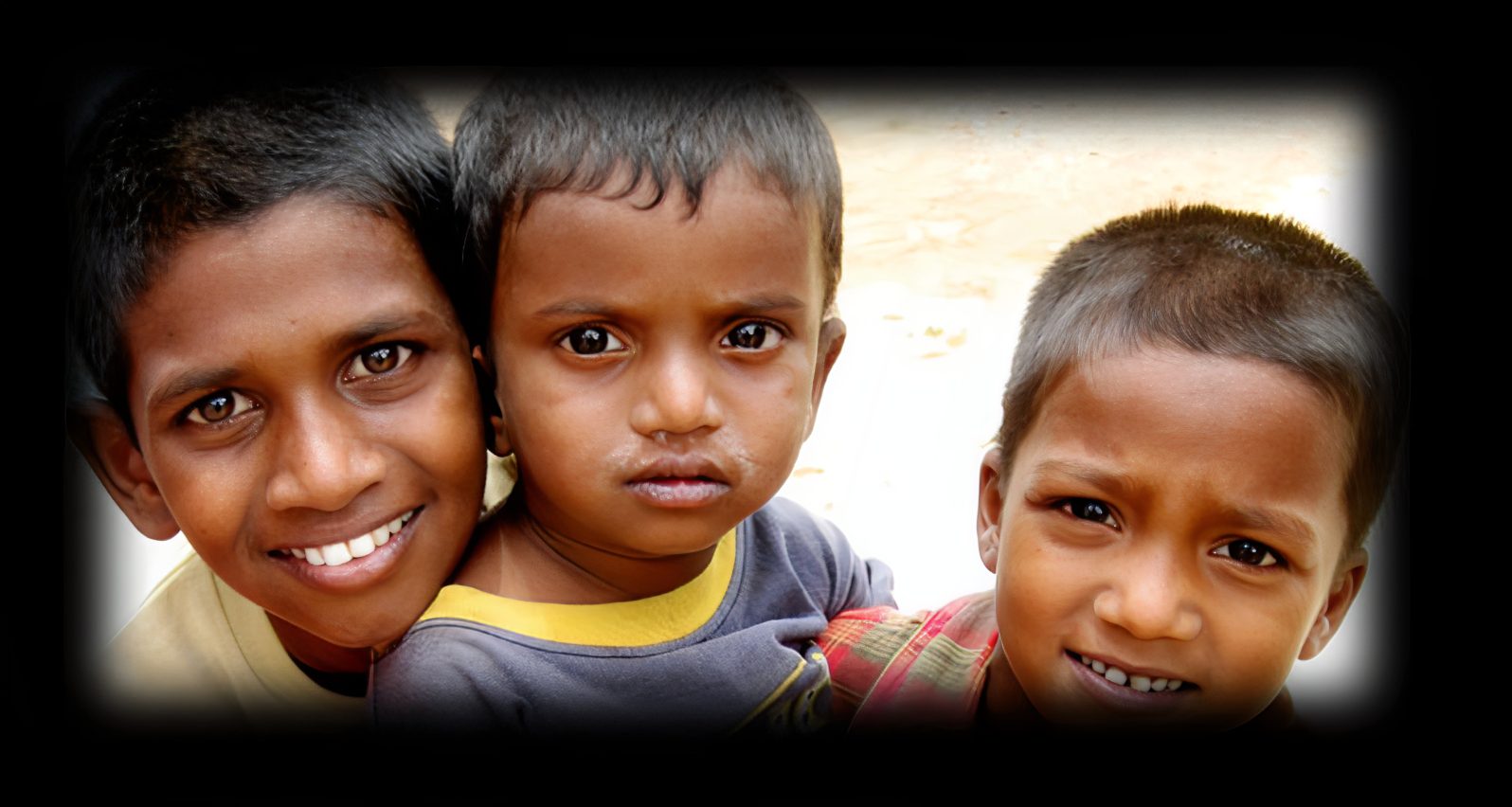 Three smiling children close together outside.